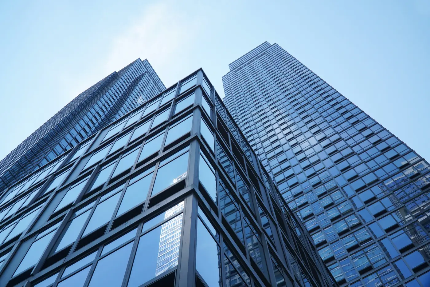 Two glass office towers rising side by side against a clear sky, symbolizing a firm and its advisory partner